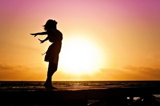 side view silhouette of girl with arms outstretched behind her in front of sunset