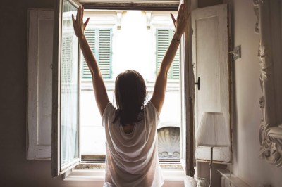 Woman's back to us with arms outstretched looking out of a window ready to face world.