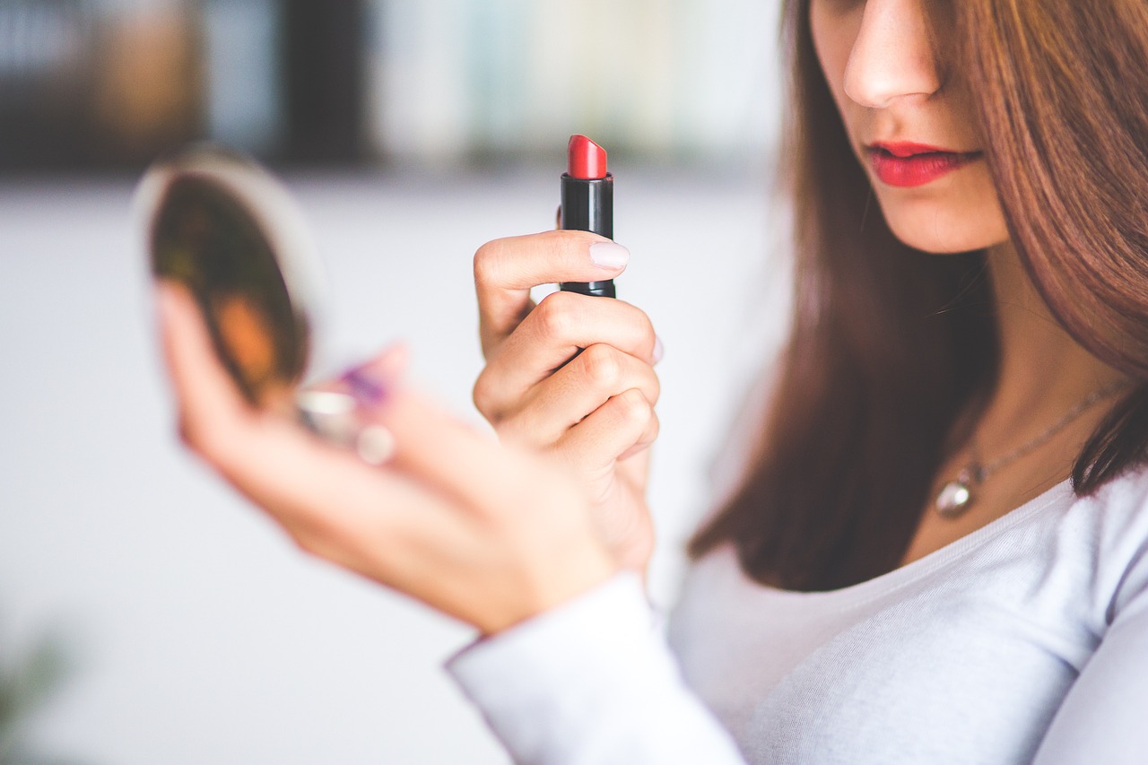 woman putting on lipstick while looking in mirror